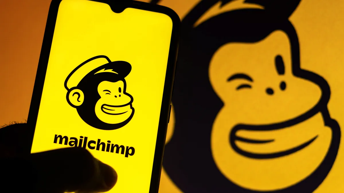 A Mailchimp logo on a phone with a larger Mailchimp in the background.